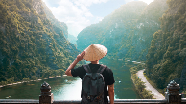 man with Vietnamese style hat is looking over the river and mountainous region